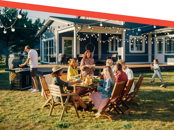 Family enjoying backyard summer barbecue and outdoor dining under string lights by modern house